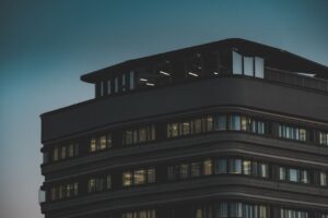 A sleek modern building with illuminated windows captured at dusk against a moody sky.